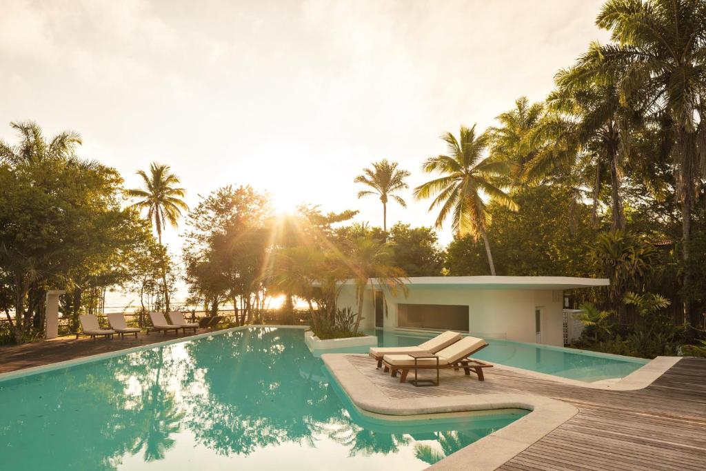 a pool with chairs and a house with palm trees at Auka Boipeba in Ilha de Boipeba