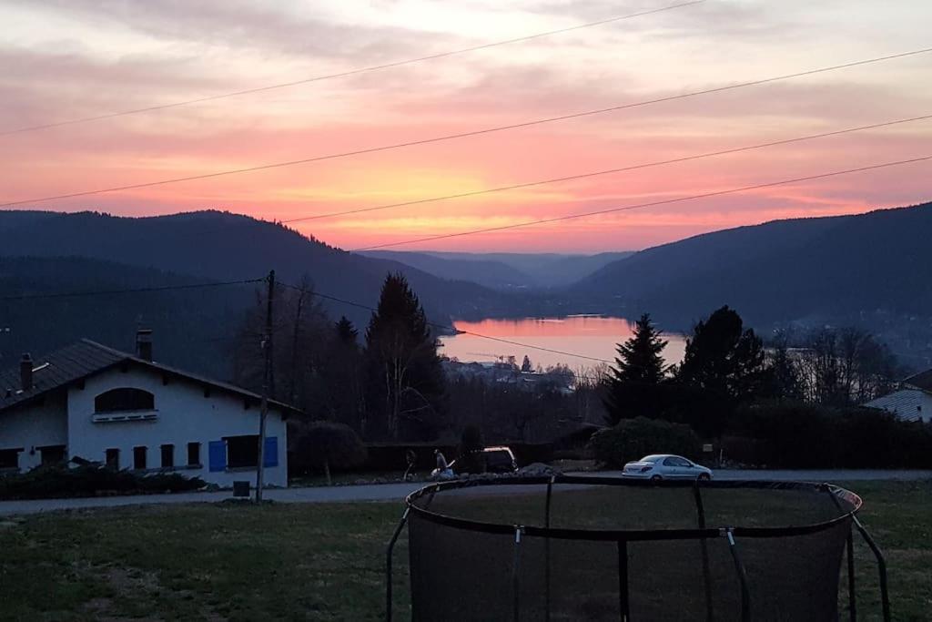 a sunset over a field with a house and a lake at Gîte Les sepneilles ! in Gérardmer