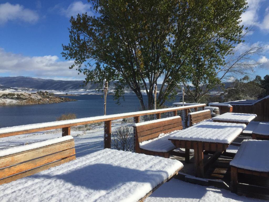 een tafel en banken bedekt met sneeuw naast een waterlichaam bij Siesta Villa in Jindabyne