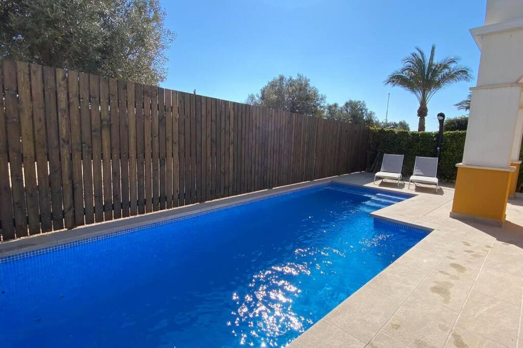 a swimming pool with two chairs next to a wooden fence at Villa Alegre - 2 bed villa with private heated pool on Mar Menor Golf - family friendly in Torre-Pacheco