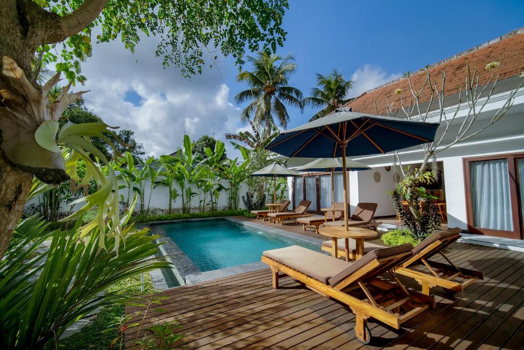 una terraza con sillas y una sombrilla junto a la piscina en Titian Dewi Villa Ubud - 3 Bedroom Private Villa Close to Cretya Day Club en Tegalalang