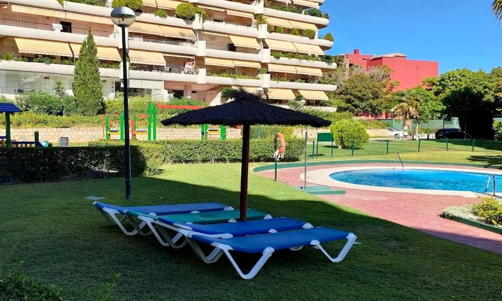 Duas espreguiçadeiras e um guarda-sol ao lado de uma piscina em Apartamento en Marbella junto a campos de golf em Marbella