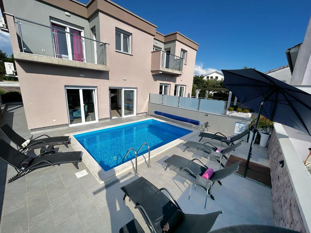 a swimming pool with chairs and an umbrella next to a house at Holiday house "Sabine pink" in Skrbčići