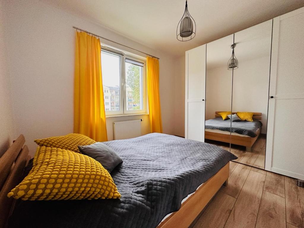 a bedroom with a bed with yellow curtains and a mirror at Apartament Neustettin-Polna Szczecinek in Szczecinek