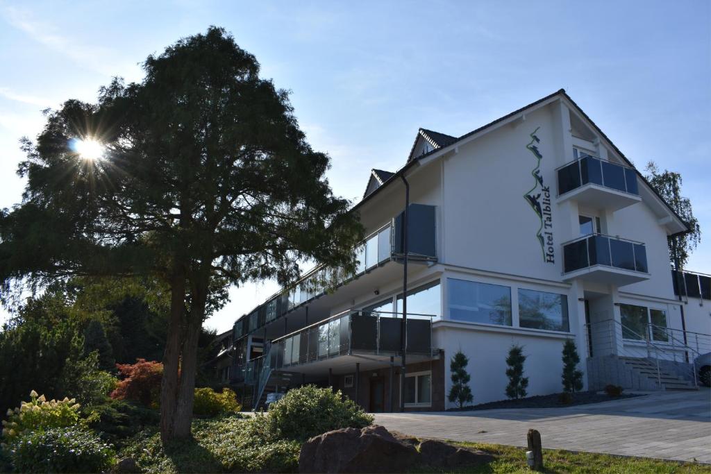 ein weißes Gebäude mit einem Baum davor in der Unterkunft Hotel Talblick in Dobel