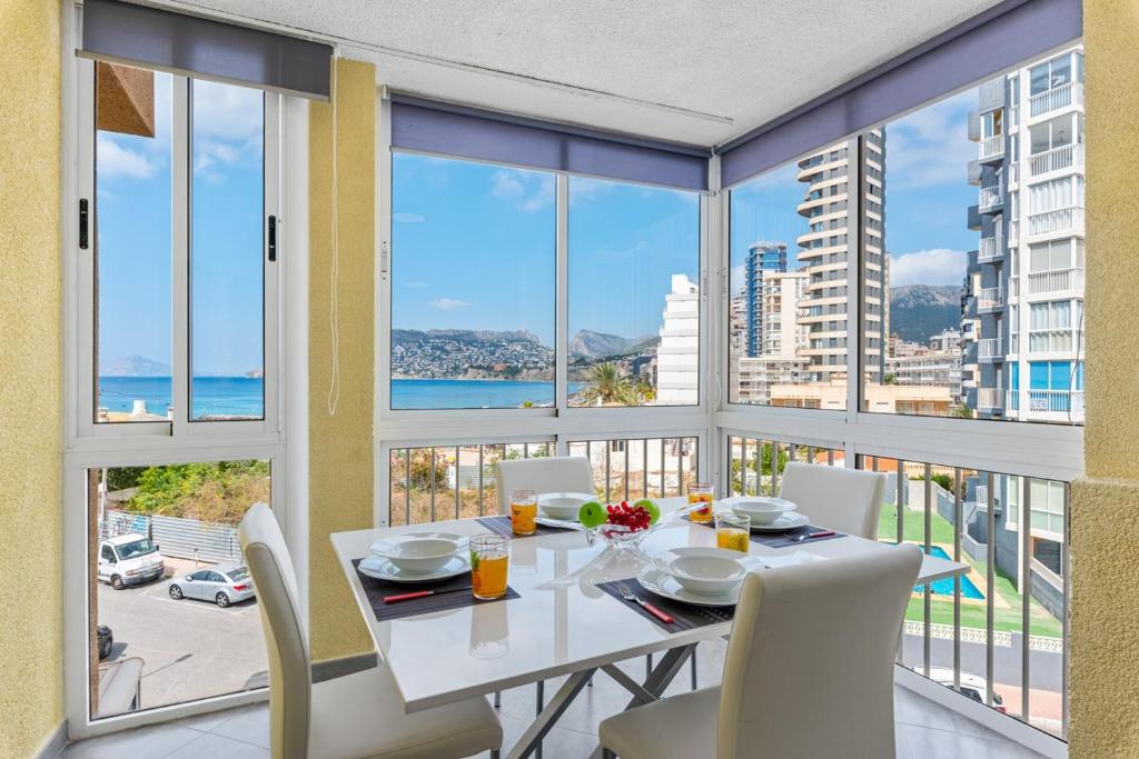 a dining room with a table and chairs and windows at Apartamento Bondi - PlusHolidays in Calpe