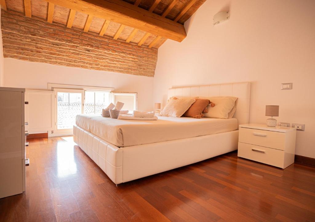 1 dormitorio con 1 cama blanca grande y suelo de madera en Mansarda storica Colombo in centro - parcheggio privato, en Ferrara
