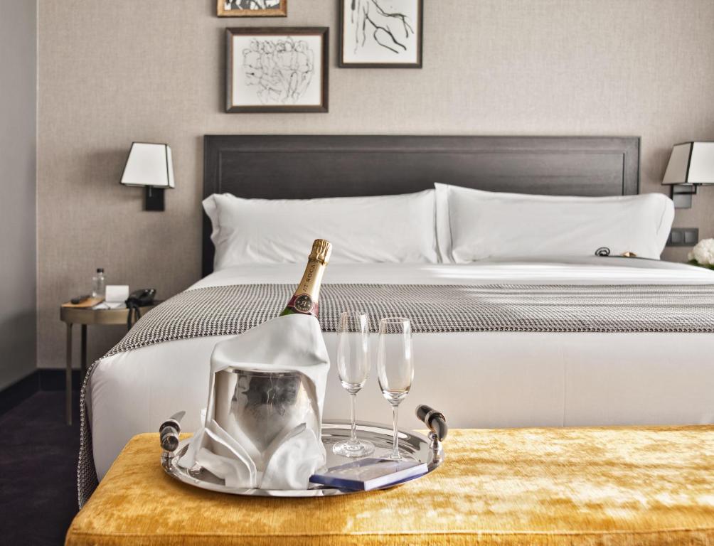 a bed with a bottle of champagne and glasses on a table at The Principal Madrid, Small Luxury Hotels in Madrid