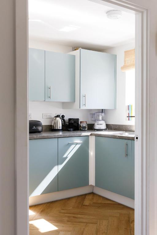 a kitchen with white cabinets and a wooden floor at Sanderling House, walk to beach in Earnley