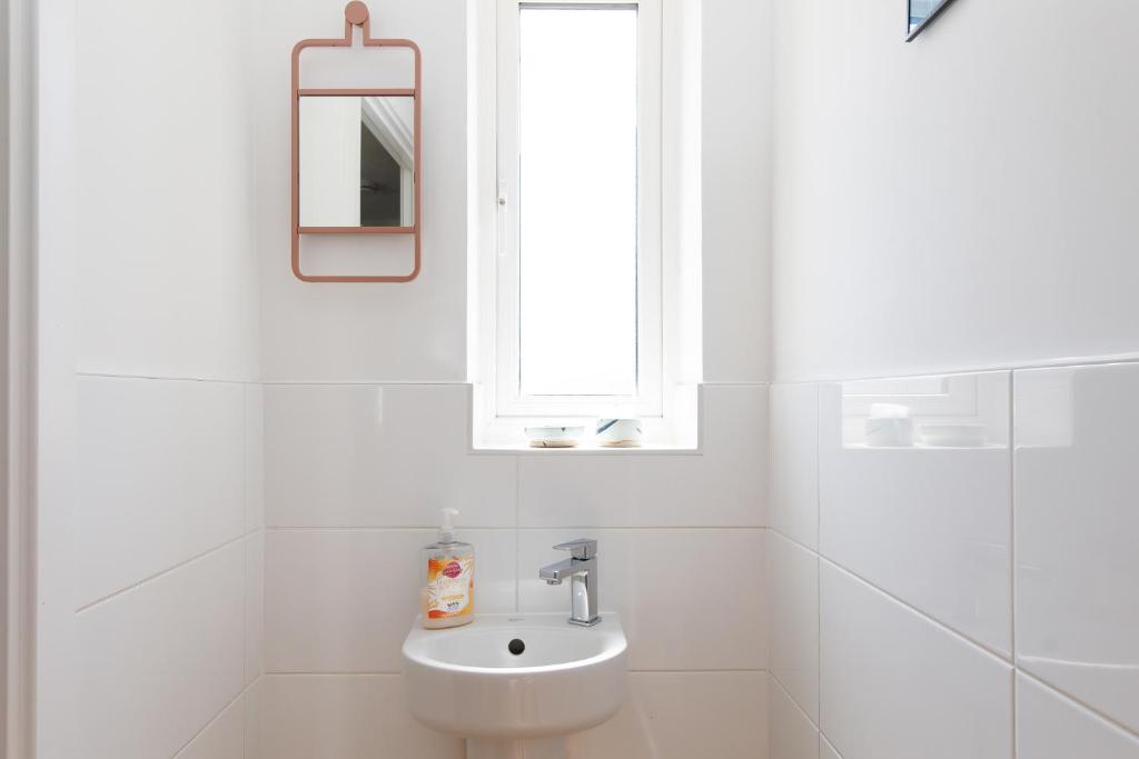 a white bathroom with a sink and a window at Sanderling House, walk to beach in Earnley