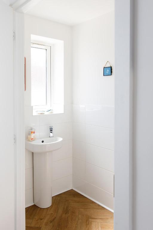 a white bathroom with a sink and a window at Sanderling House, walk to beach in Earnley