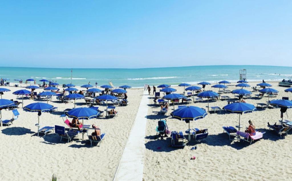 een strand met blauwe parasols en mensen op het zand bij Appartamento AL FARO in Alba Adriatica