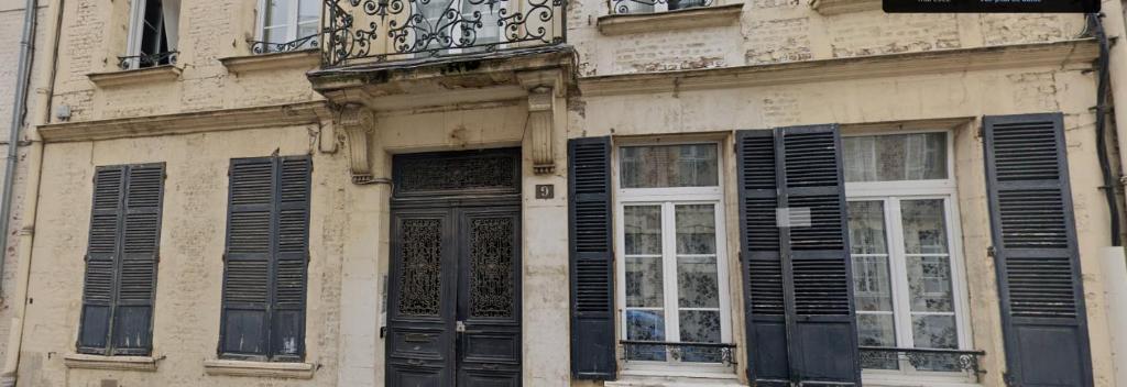 um edifício com janelas com persianas pretas e uma varanda em Le Voltaire 4 chez Adrien Hyper centre em Saint-Quentin