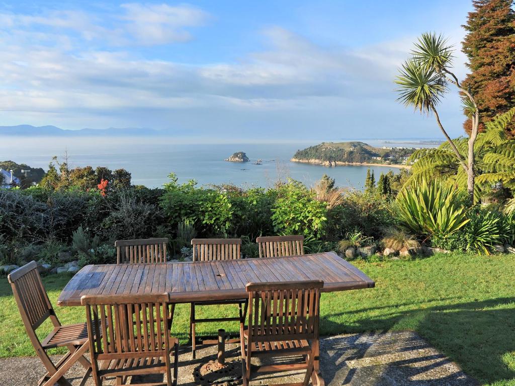 a wooden table with three chairs and a view of the ocean at Kereru at Kaiteriteri - Kaiteriteri Holiday Home in Kaiteriteri
