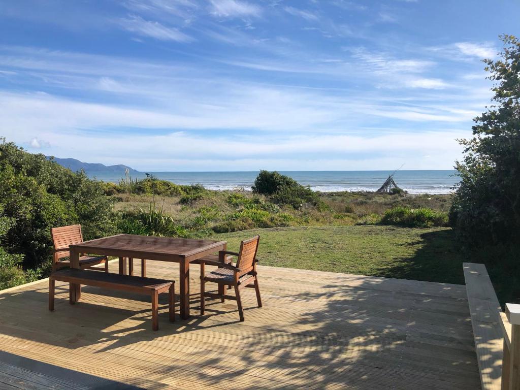 een houten tafel en stoelen op een terras met het strand bij The Beachsider - Te Horo Beach Holiday Home in Te Horo
