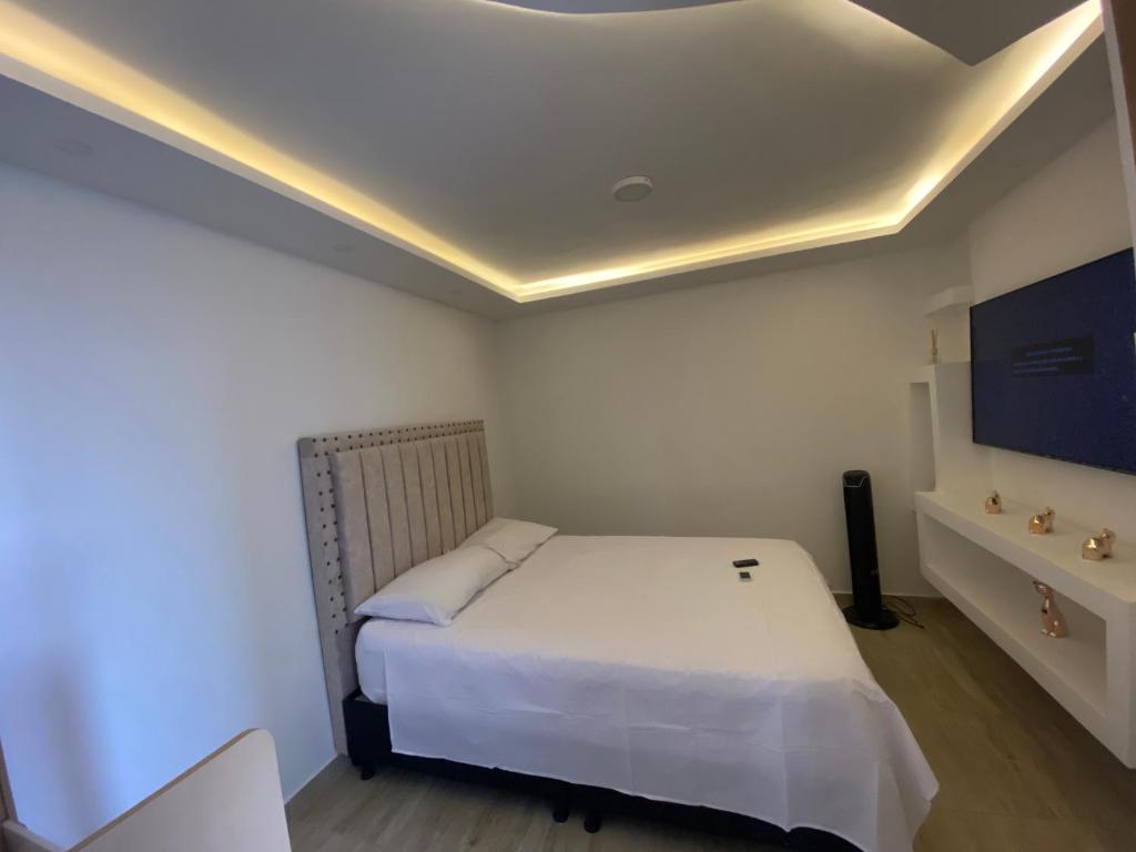 een slaapkamer met een wit bed en een televisie bij Hermoso apartamento a solo 15 minutos del parque del cafe in Montenegro