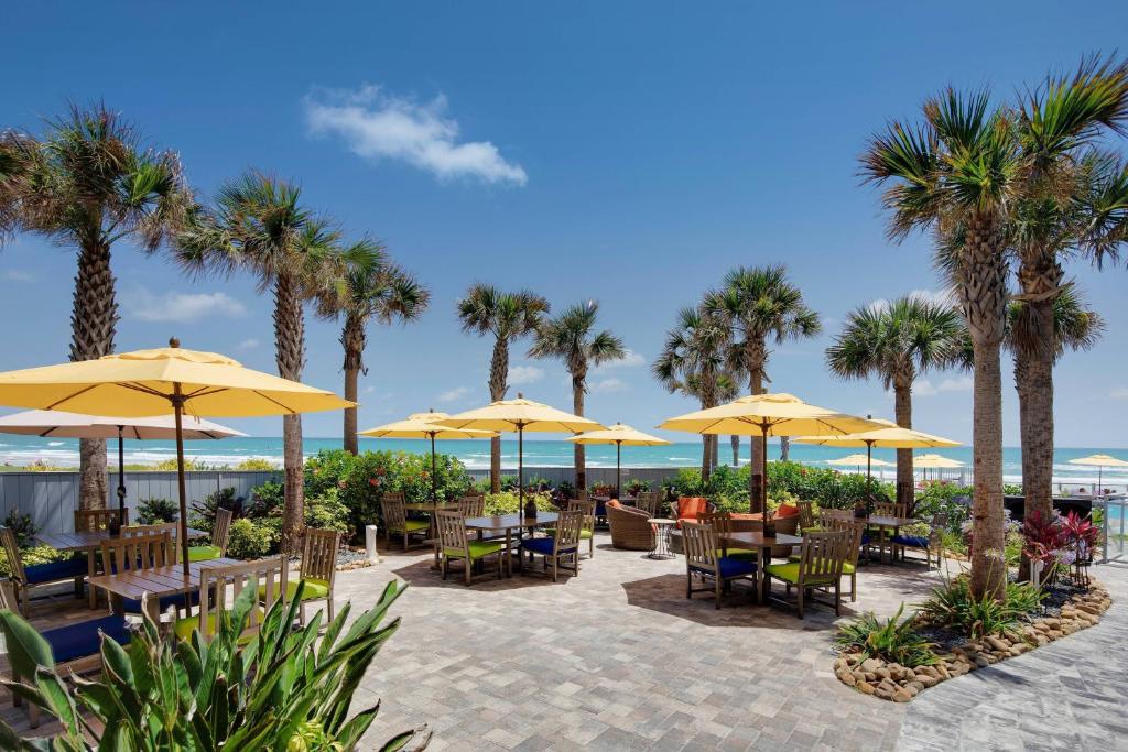 a patio with tables and umbrellas and palm trees at Delta Hotels by Marriott Daytona Beach Oceanfront in Daytona Beach