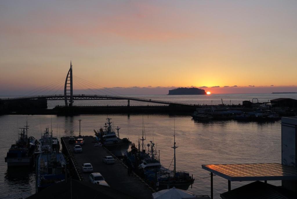 a sunset with a bridge and boats in the water at Soldongsan Stay in Seogwipo