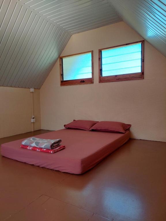 ein großes Bett in einem Zimmer mit zwei Fenstern in der Unterkunft Le chalet Scarlet in Teahupoo