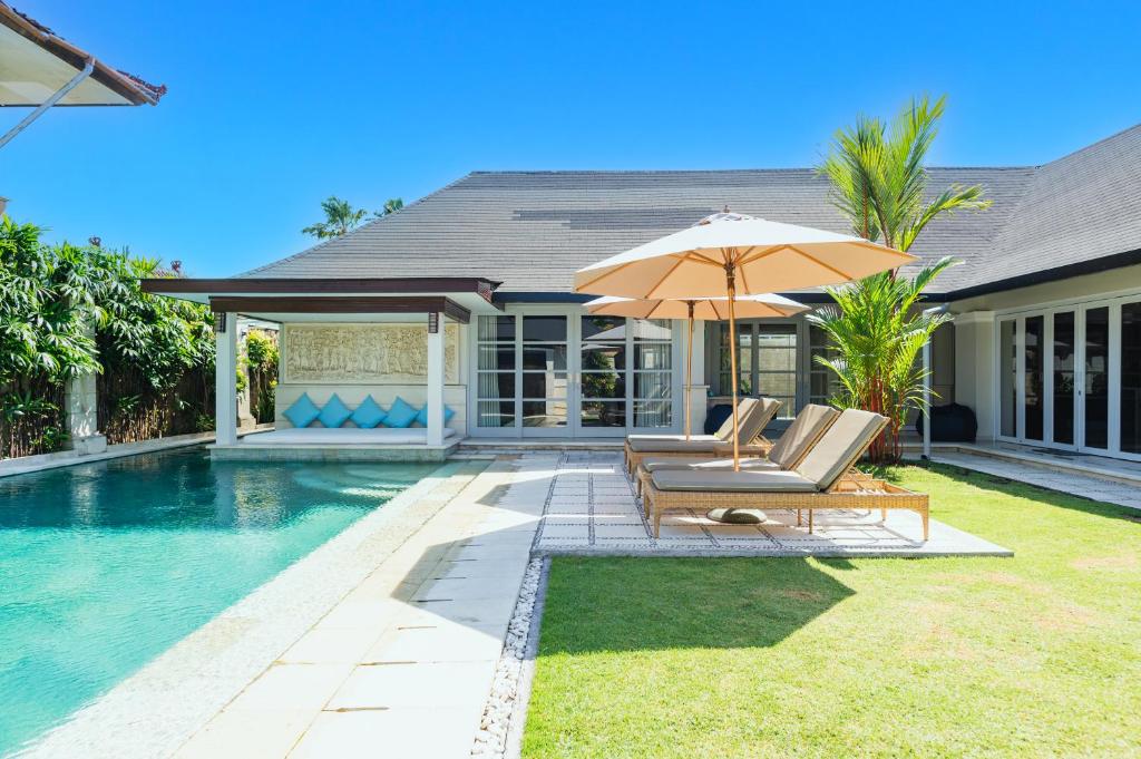 uma piscina com duas cadeiras e um guarda-sol ao lado de uma casa em The Zen Villas em Sanur