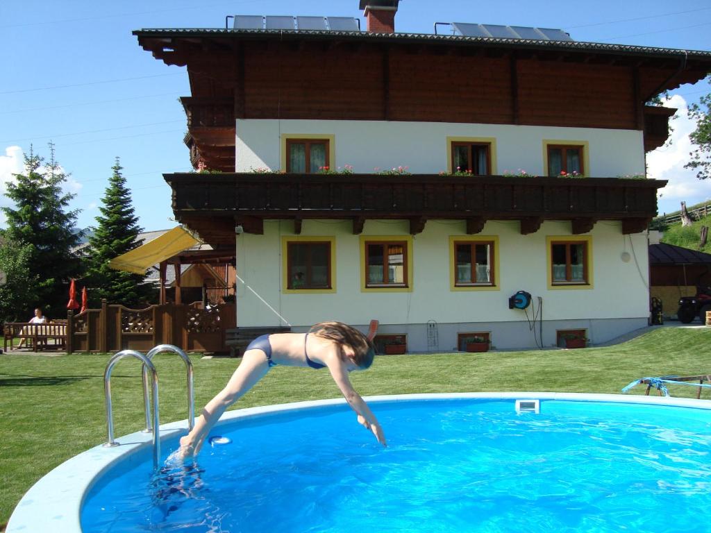 Hotel - Pension Ötzmooshof في سانكت يوهان ايم بونغ: امرأة تقفز في حمام السباحة أمام المنزل