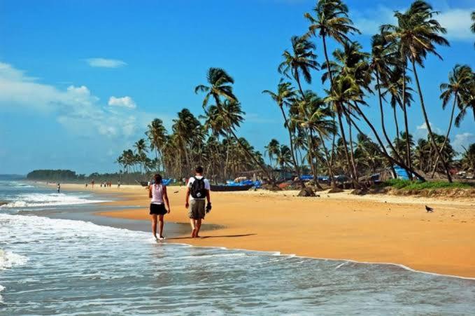 two people walking on a beach with palm trees at Baga Beach Prime in Baga