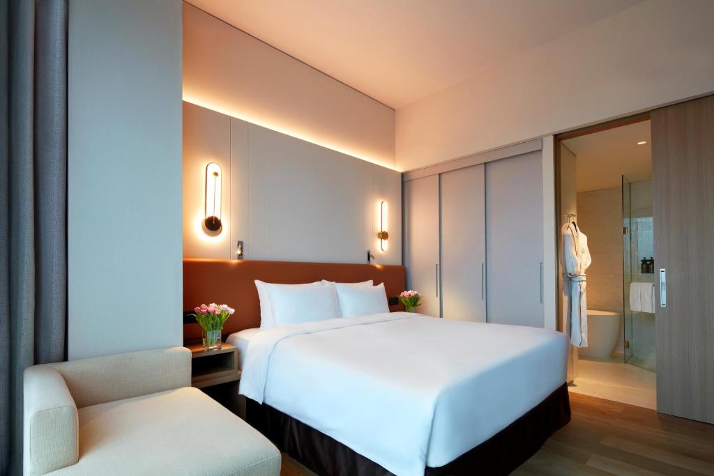 a bedroom with a large white bed and a chair at Momentus Hotel Alexandra in Singapore