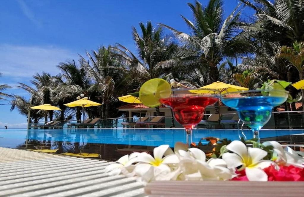 two martini glasses sitting next to a swimming pool at Saigon Emerald Beach Resort in Mui Ne