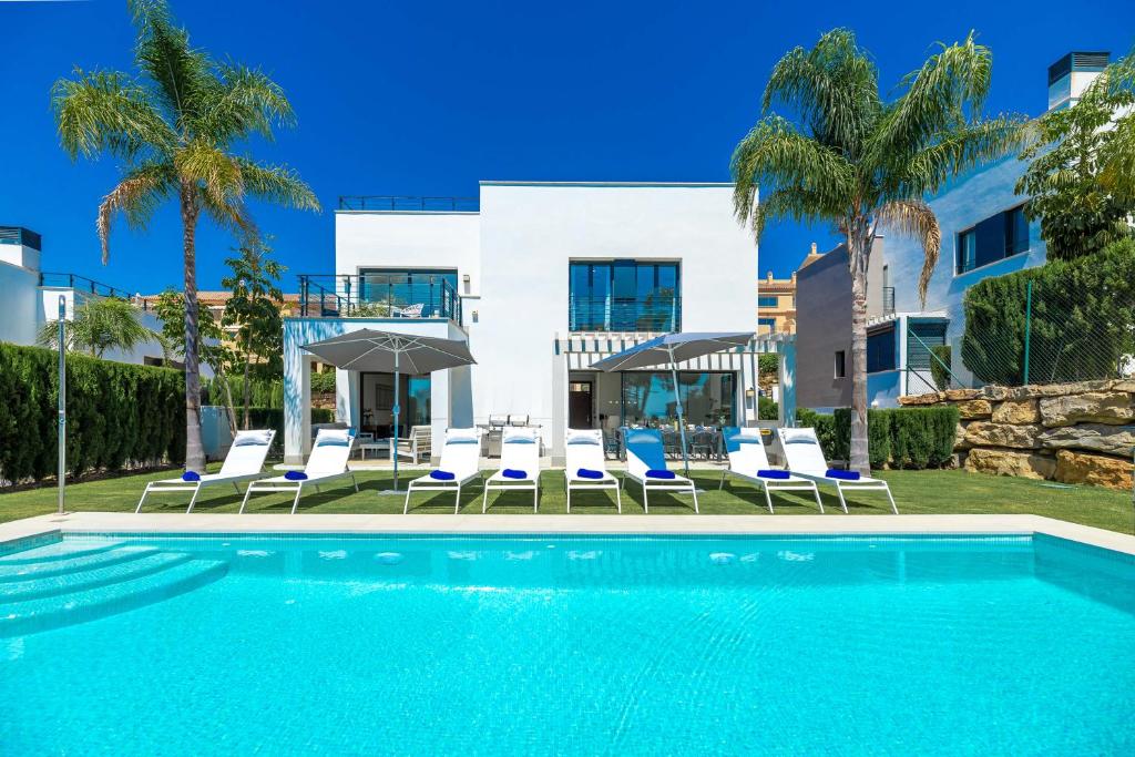 a pool with chairs and umbrellas in front of a building at VACATION MARBELLA I Villa Chloe The Golfer, Infinity Pool, Rooftop Views, New-Built in Estepona