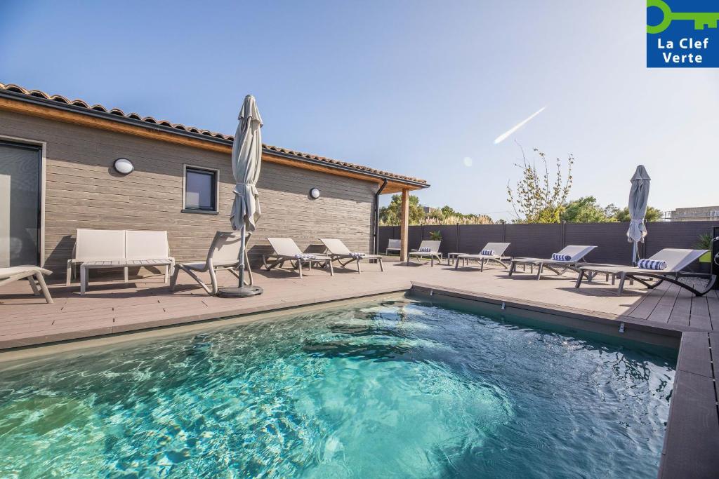 a swimming pool with chairs and umbrellas next to a house at Résidence Pierre & Vacances Premium Vesna Rossa in Porto-Vecchio