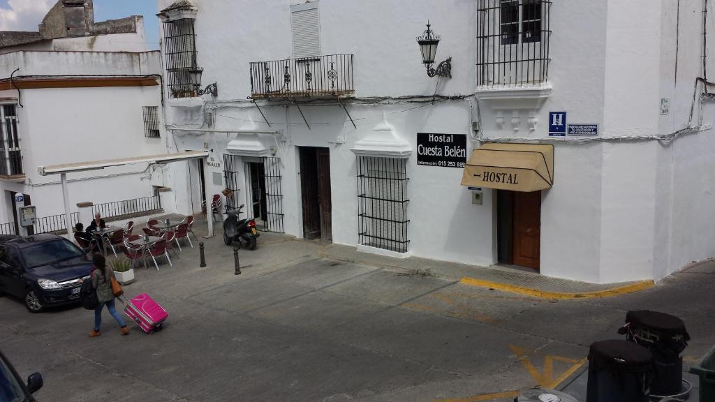 a woman walking down a street with luggage in front of a building at Hostal Cuesta de Belén in Arcos de la Frontera