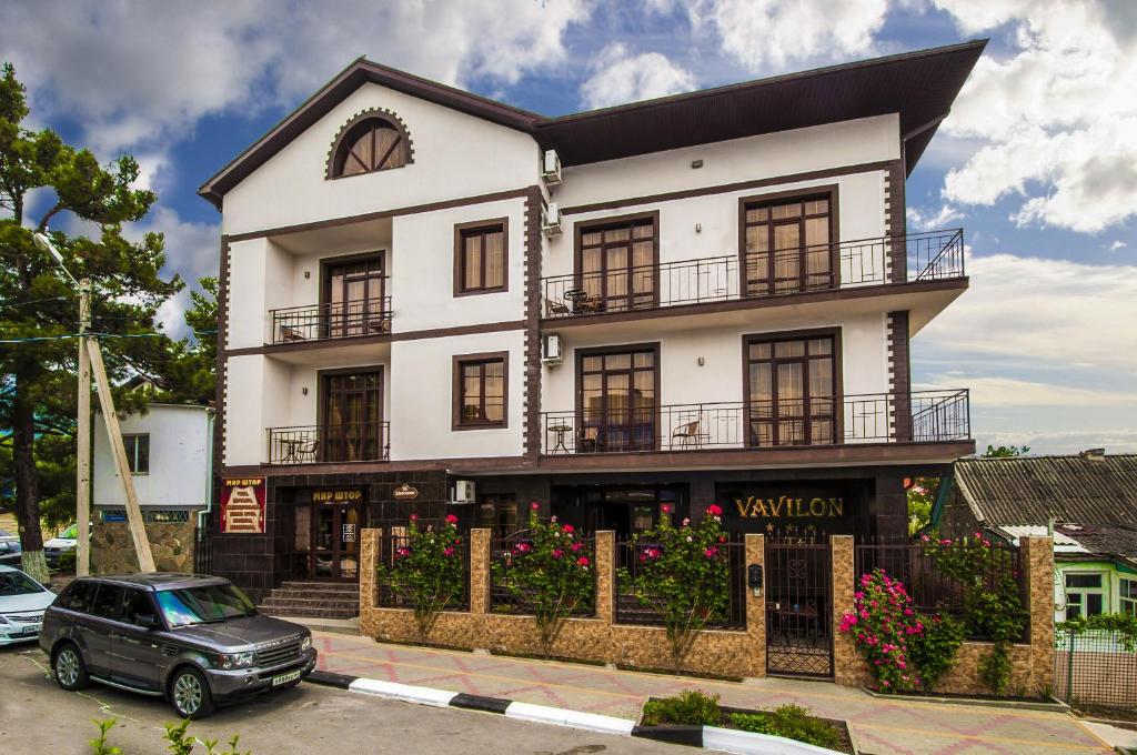 a white building with a car parked in front of it at Vavilon Hotel in Gelendzhik