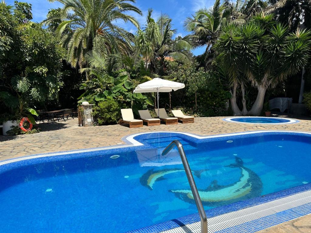 a blue swimming pool with an umbrella and palm trees at Tijarafe 2 in Tijarafe