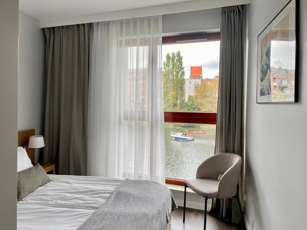 a bedroom with a bed and a window with a chair at EGH Waterlane Island Apartment in Gdańsk