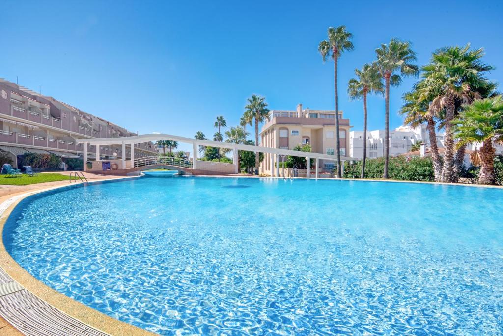 une grande piscine bordée de palmiers et un bâtiment dans l'établissement Ca Blanca Paraíso ll, à Dénia