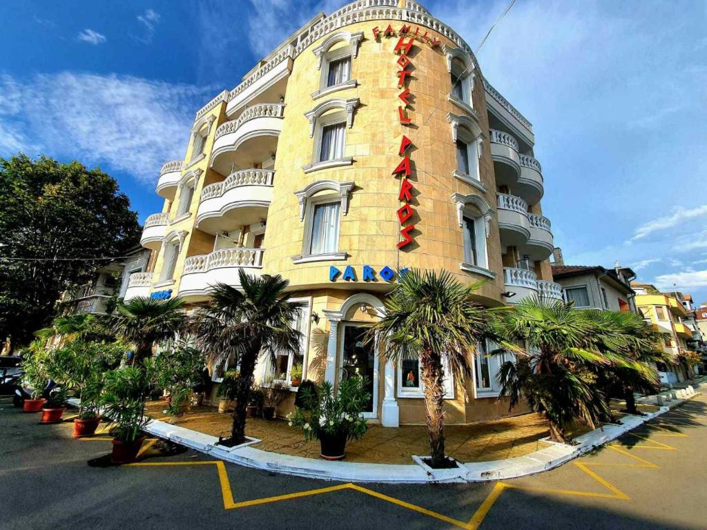 a large yellow building with palm trees in front of it at Family Hotel Paros in Pomorie