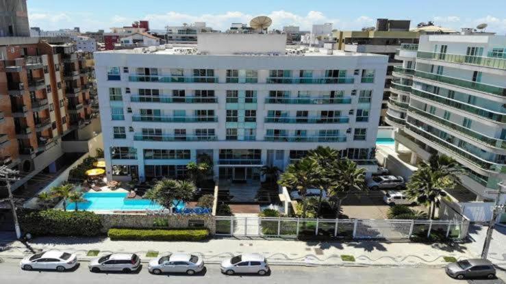 Un gran edificio blanco con coches aparcados en un estacionamiento. en MANDAI FLAT 412, en Cabo Frío
