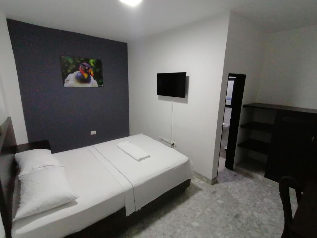 um quarto com uma cama branca e uma televisão em Hotel Bucare em Yopal