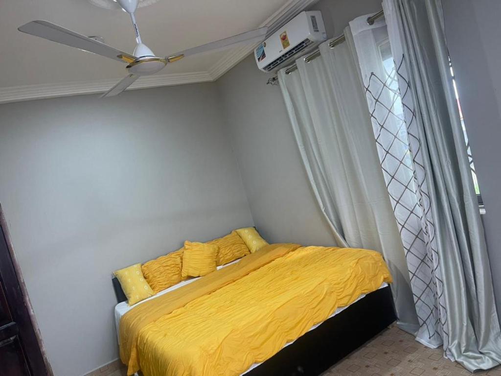 um quarto com uma cama amarela e uma ventoinha de tecto em MED COZY FLAT GH em Acra