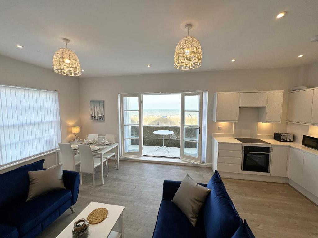 a living room with a blue couch and a kitchen at Beachfront Bliss Apartment - Near Hythe - On Beach Seafront - Private Parking in Dymchurch