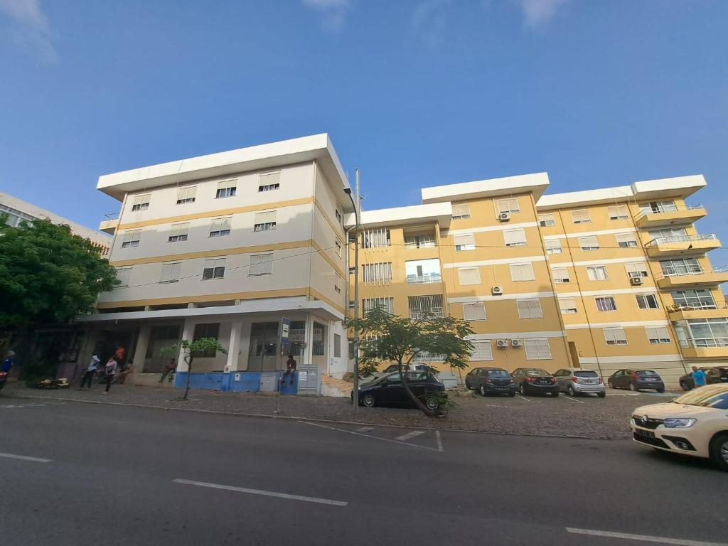 duży budynek apartamentowy z samochodami zaparkowanymi przed nim w obiekcie Quarto amplo do apartamento no Palmarejo w mieście Praia