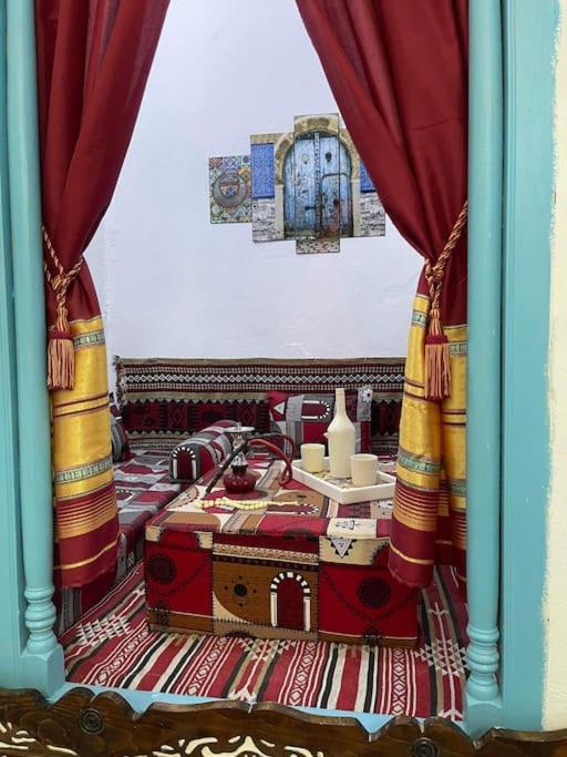 Zimmer mit einem Bett mit roten Vorhängen und einem Tisch in der Unterkunft Dar Lella Hasna in Sfax