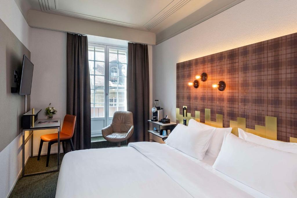 ein Hotelzimmer mit einem großen Bett und einem Schreibtisch in der Unterkunft NH Bern The Bristol in Bern