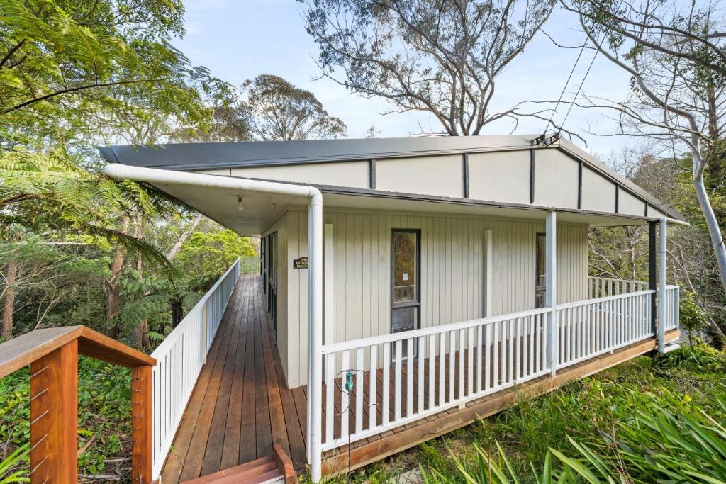 uma pequena casa branca com um deque de madeira em Tree Tops Katoomba em Katoomba