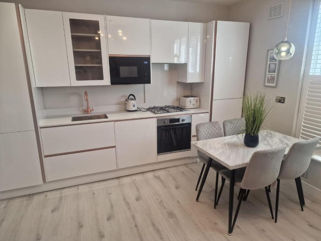 eine Küche mit weißen Schränken und einem Tisch mit Stühlen in der Unterkunft Collier's Wood en-suite apartments in London