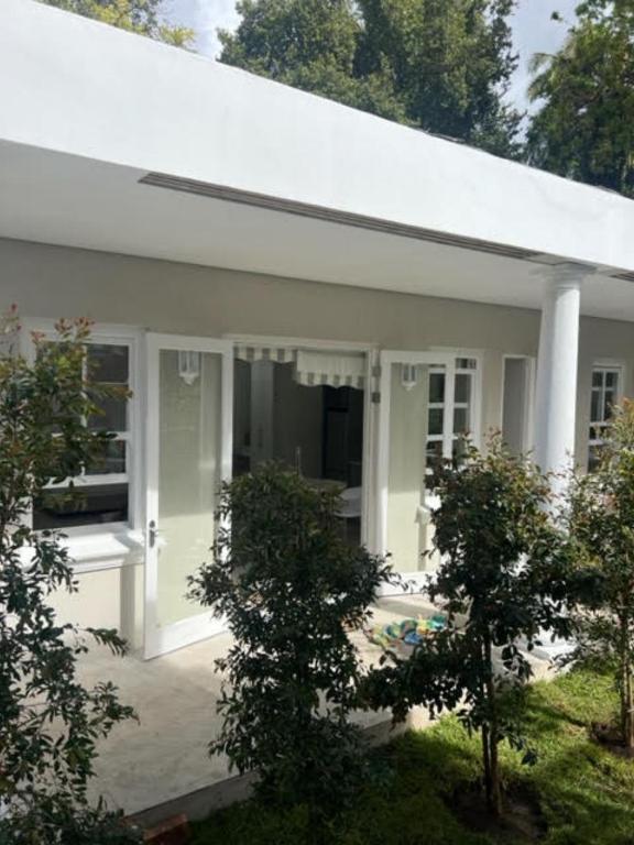 a white house with a porch and trees at Two on Milner - OAK TREE COTTAGE - Stylish open-plan Guesthouse in Rondebosch in Cape Town