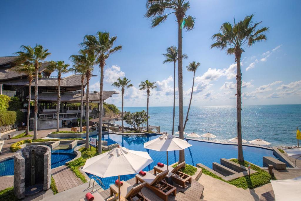 una piscina del resort con sedie, palme e l'oceano di Nora Buri Resort & Spa - SHA Extra Plus a Chaweng Beach