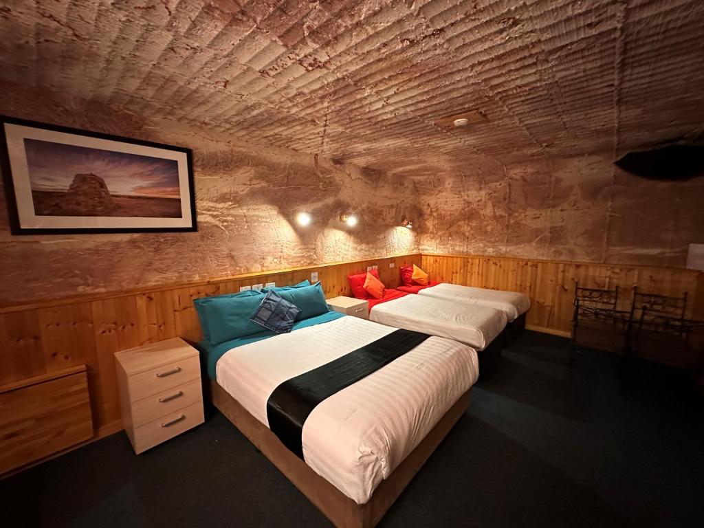 1 dormitorio con 2 camas en una pared de piedra en Comfort Inn Coober Pedy Experience, en Coober Pedy