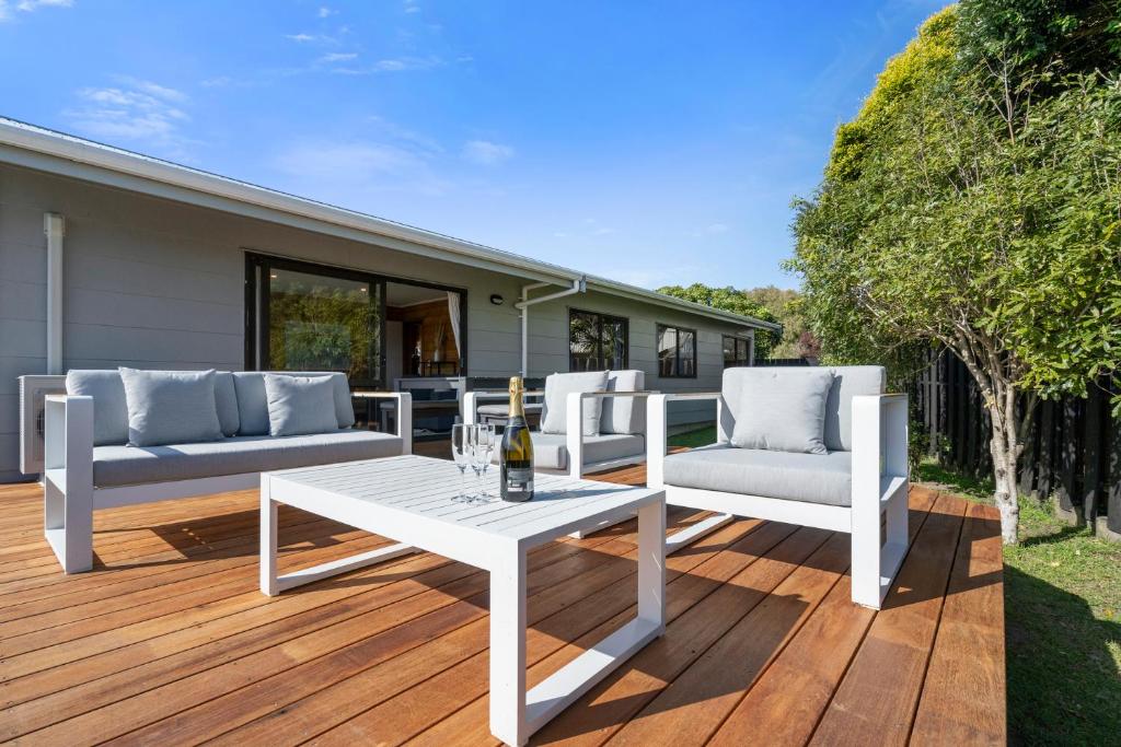 una mesa blanca y sillas en una terraza de madera en Sunset Cottage - Waikanae Beach Holiday Home, en Waikanae