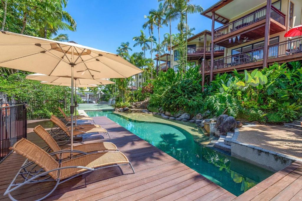 a pool with chairs and an umbrella on a wooden deck at The Point Villa 10 in Port Douglas